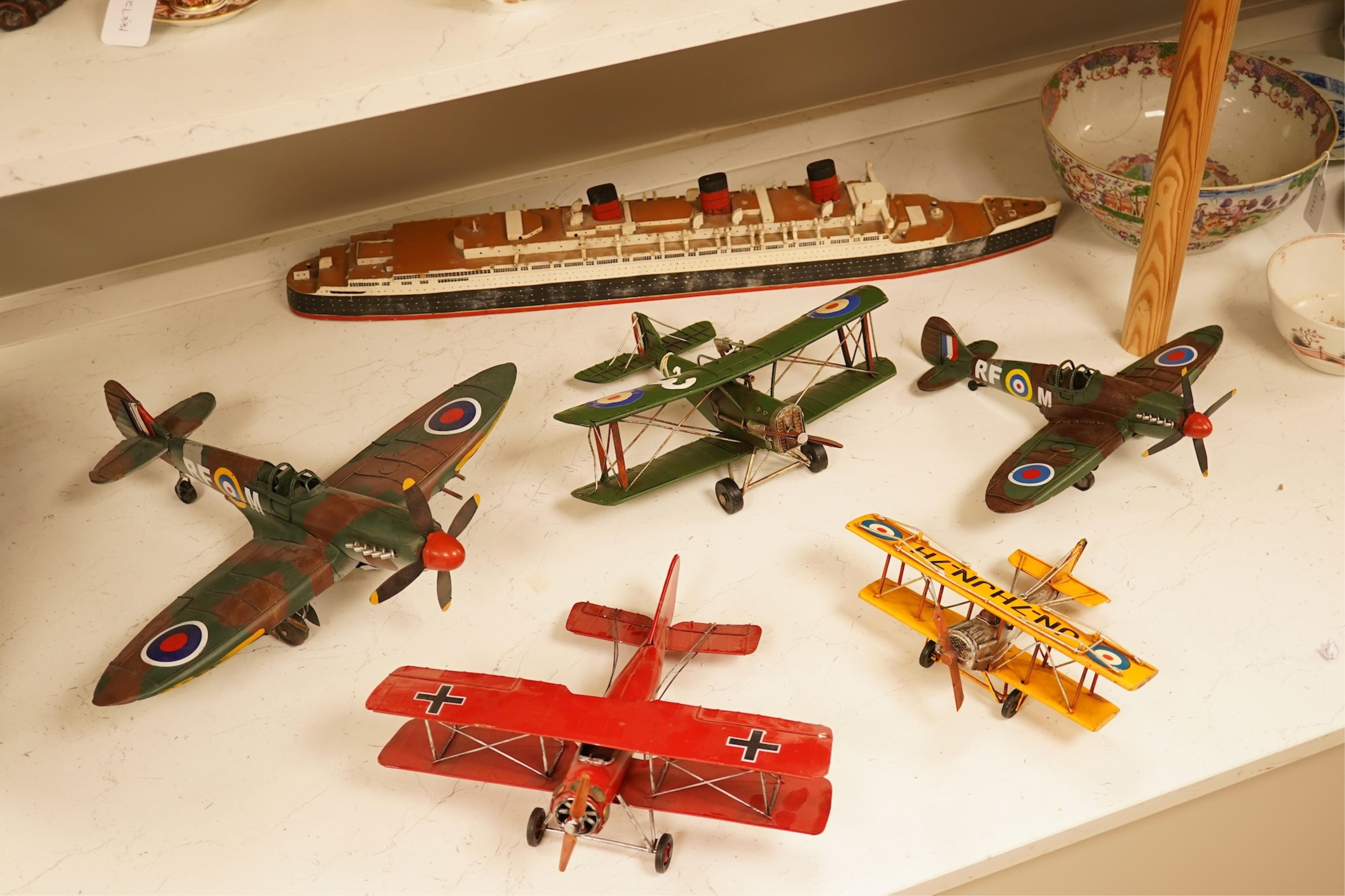 Five decorative metal models of military aircraft, including two Supermarine Spitfires, two First World War, British bi-planes, a German Albatros D.III bi-plane, and a wooden model of RMS Queen Mary, hull 77cm long